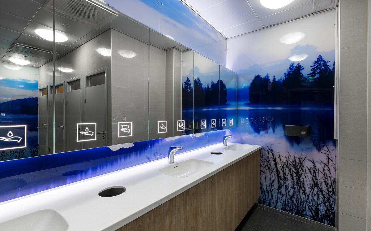 Novosan referenssi. Kauppakeskus Goodmanin WC-tila. Vessassa on kolme käsienpesupaikkaa ja peilikaapit. Vessan seinäpinta-alan täyttää sinisen sävyinen luontokuva.