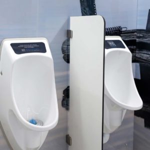 Vedettömät Urimat-pisuaarit EcoPlus ja CompactPlus miesten vessassa. Kaksi valkoista Ujo-väliseinää rajaavat sinertävää tilaa.