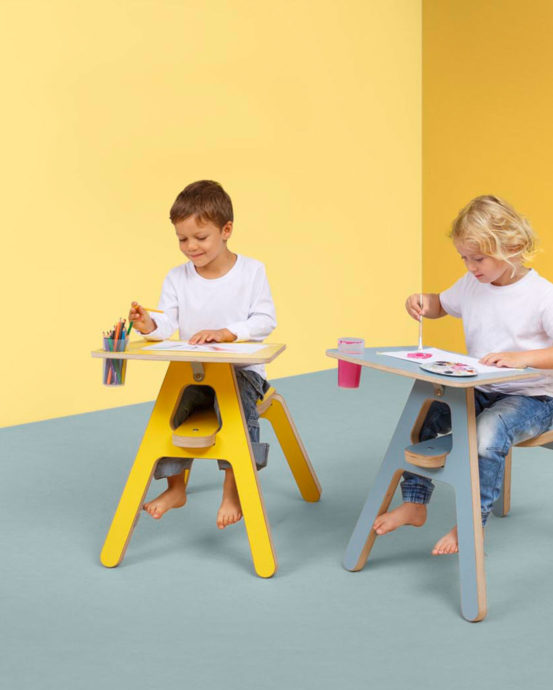 Lapset piirtävät ja maalaavat Novosan Timkid Clexo-piirtopöydissä. Pieni poika värittää puukynillä ja pieni tyttö maalaa vesiväreillä. Huoneen seinät ovat keltaiset. Poika istuu keltaisessa piirtopöytä- ja tuoliyhdistelmässä, tyttö harmaassa. Lapsilla on paljaat jalat.