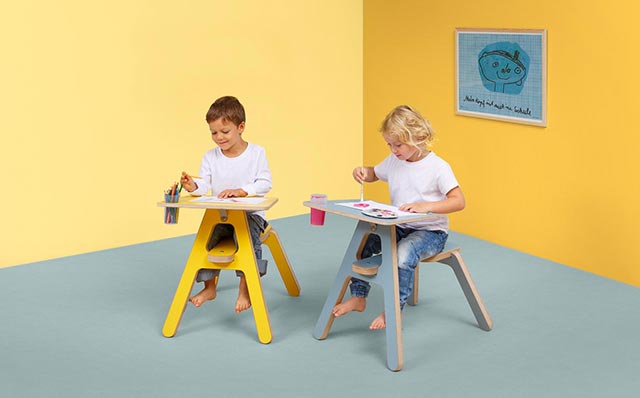 Lapset piirtävät ja maalaavat Novosan Timkid Clexo-piirtopöydissä. Pieni poika värittää puukynillä ja tyttö maalaa vesiväreillä. Piirtopöytien värit: harmaa ja keltainen.
