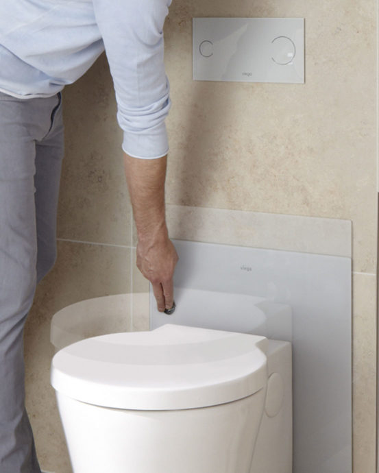 Vaaleassa WC-tilassa mies painaa korkeussäädettävän seinä-WC-istuin, huuhtelunappia. Kuvassa epätarkkana liikkeenä WC-istuimen laskeutuminen.