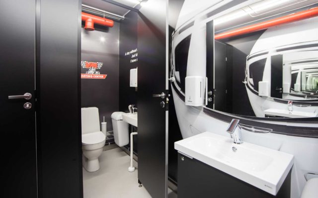 Mustavalkoisessa WC-tilassa on Conti+ ultra - hana ja valkoinen lavuaari, jonka yläpuolella on kaareva peili. Seinään on myös kiinnitetty saippua-annostelija ja vaatekoukku. Valkoinen WC-pönttö ja WC-kalusteet näkyvät toisessa eriössä, jonka ovi on auki.