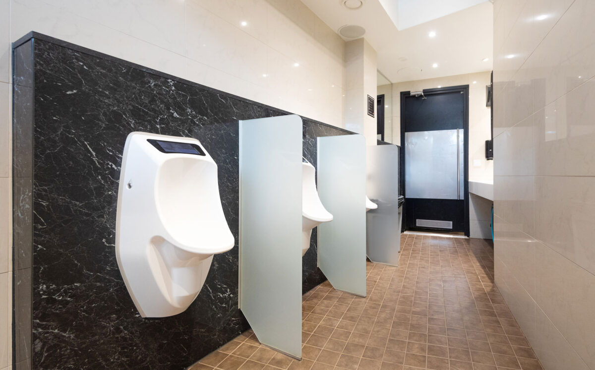 Miesten WC-tila. Valkoiset urinaalit ja väliseinät on kiinnitetty mustaan marmoriseen paneeliin.