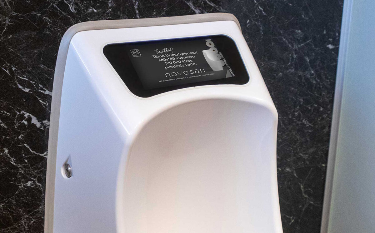 Urinaali ja LCD-videonäyttö. Näytössä lukee: Tiesitkö? Tämä Urimat-pisuaari säästää vuodessa 100 000 litraa puhdasta vettä.