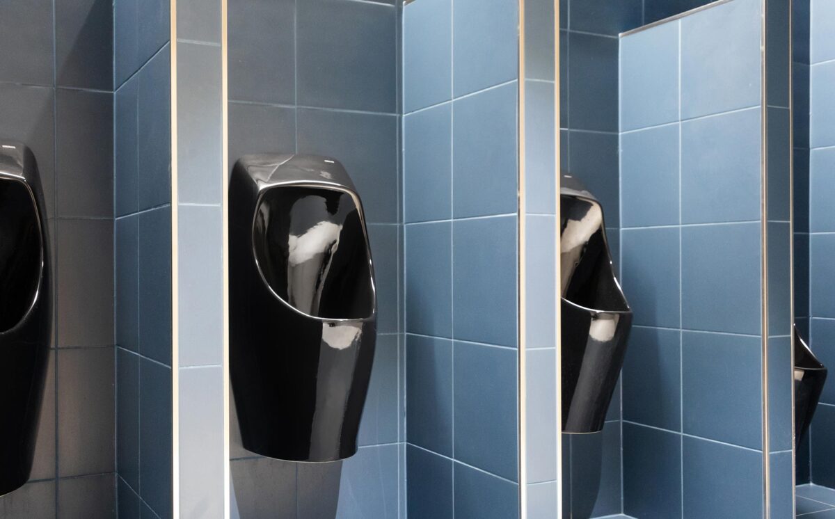 Neljä mustaa vedetöntä Urimat-urinaalia sinisen sävyisessä miesten WC:ssä.