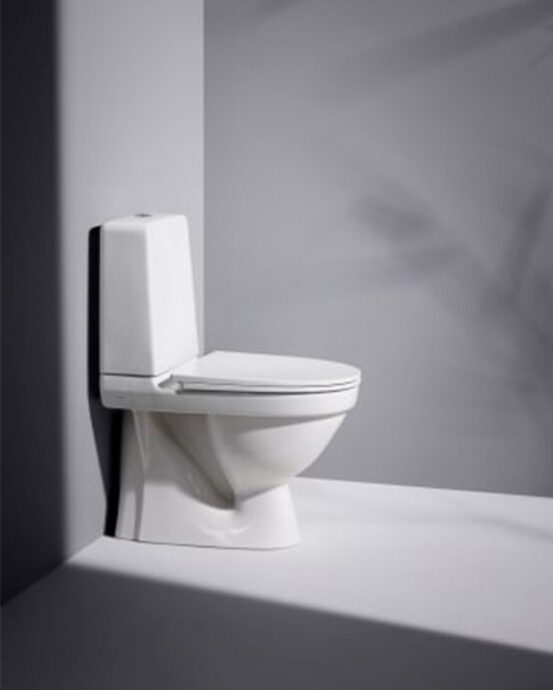 Kuvassa valkoinen Laufen Kompas -WC-istuin sivusta kuvattuna. WC-tilassa harmaat seinät ja lattia.