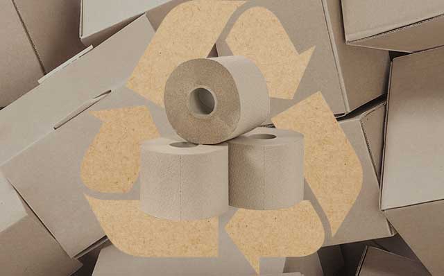 Kierrätyskuiduista valmistettuja paperirullia kierrätyspahvin päällä, taustalla kierrätyssymboli, joka havainnollistaa materiaalien uudelleenkäyttöä ja kiertotaloutta.